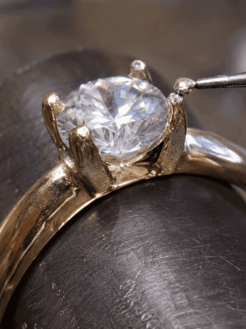 Jeweler's torch flame heating a gold solitaire diamond ring held in a bench clamp with tweezers