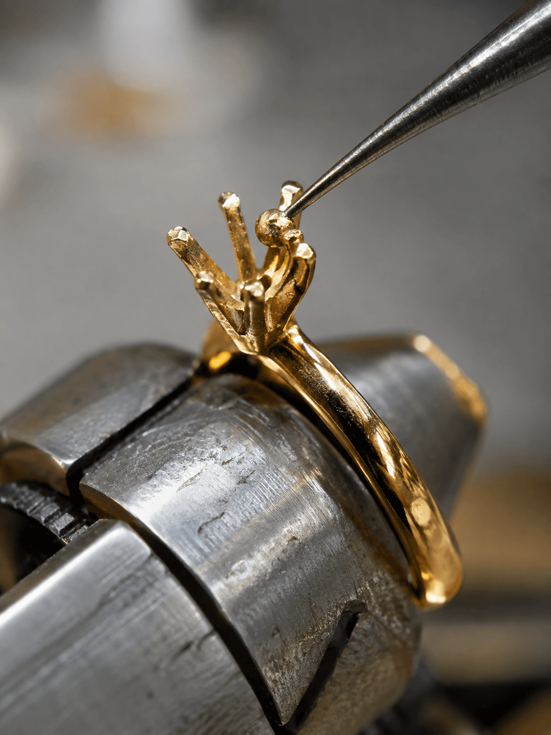 Jeweler's pick tool adjusting prongs on a gold solitaire ring clamped in a bench vise