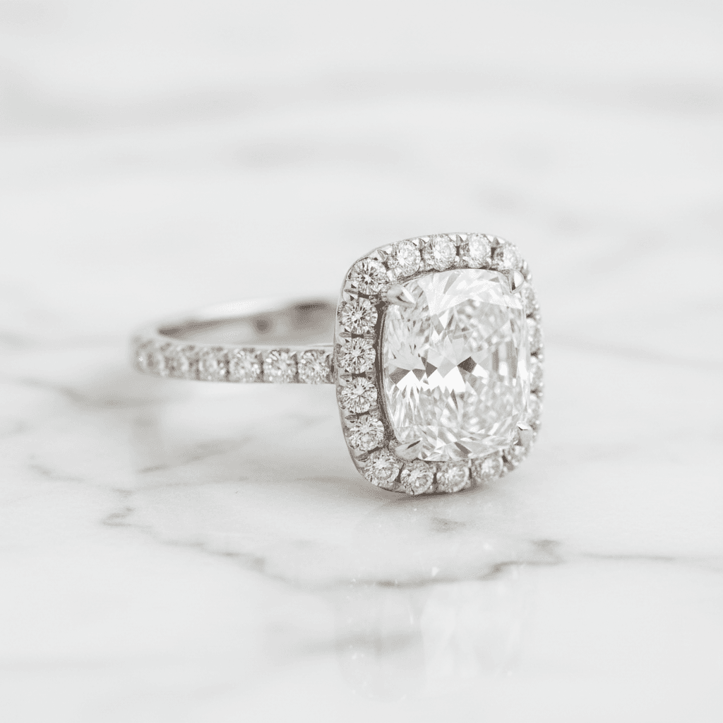 Cushion-cut diamond halo engagement ring with pavé band on white marble