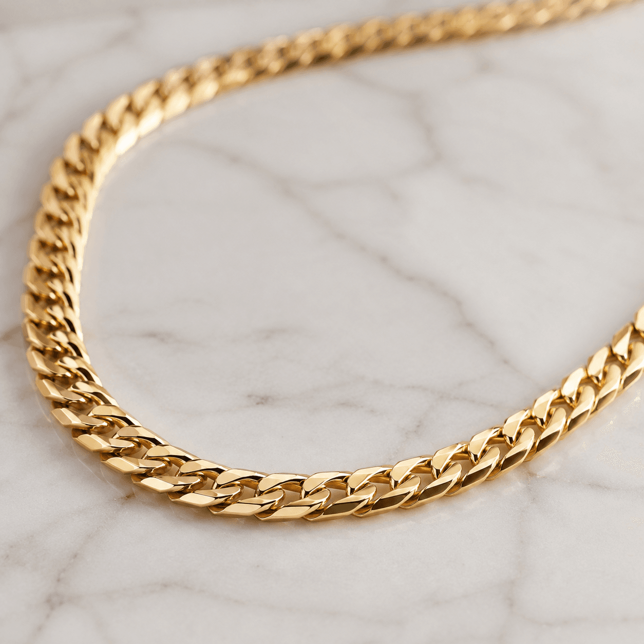 A finished, polished gold chain necklace draped elegantly over a white marble surface, warm natural light catching the