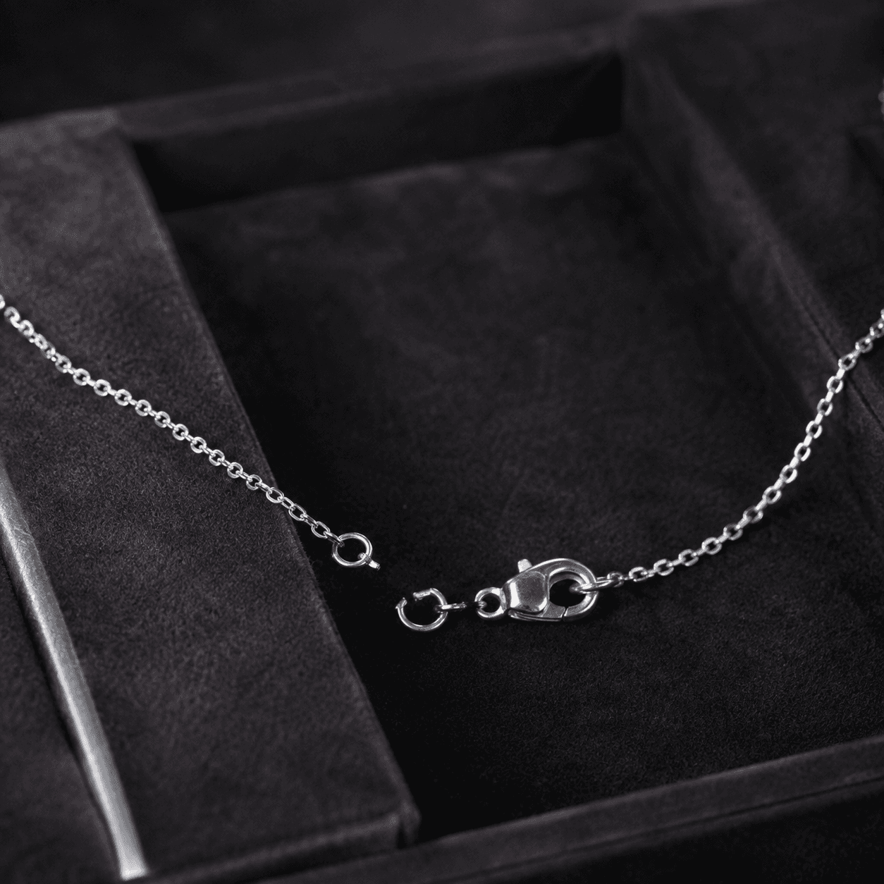 A delicate platinum necklace with a damaged clasp laid flat on a dark velvet jeweler's tray, soft overhead studio lighting