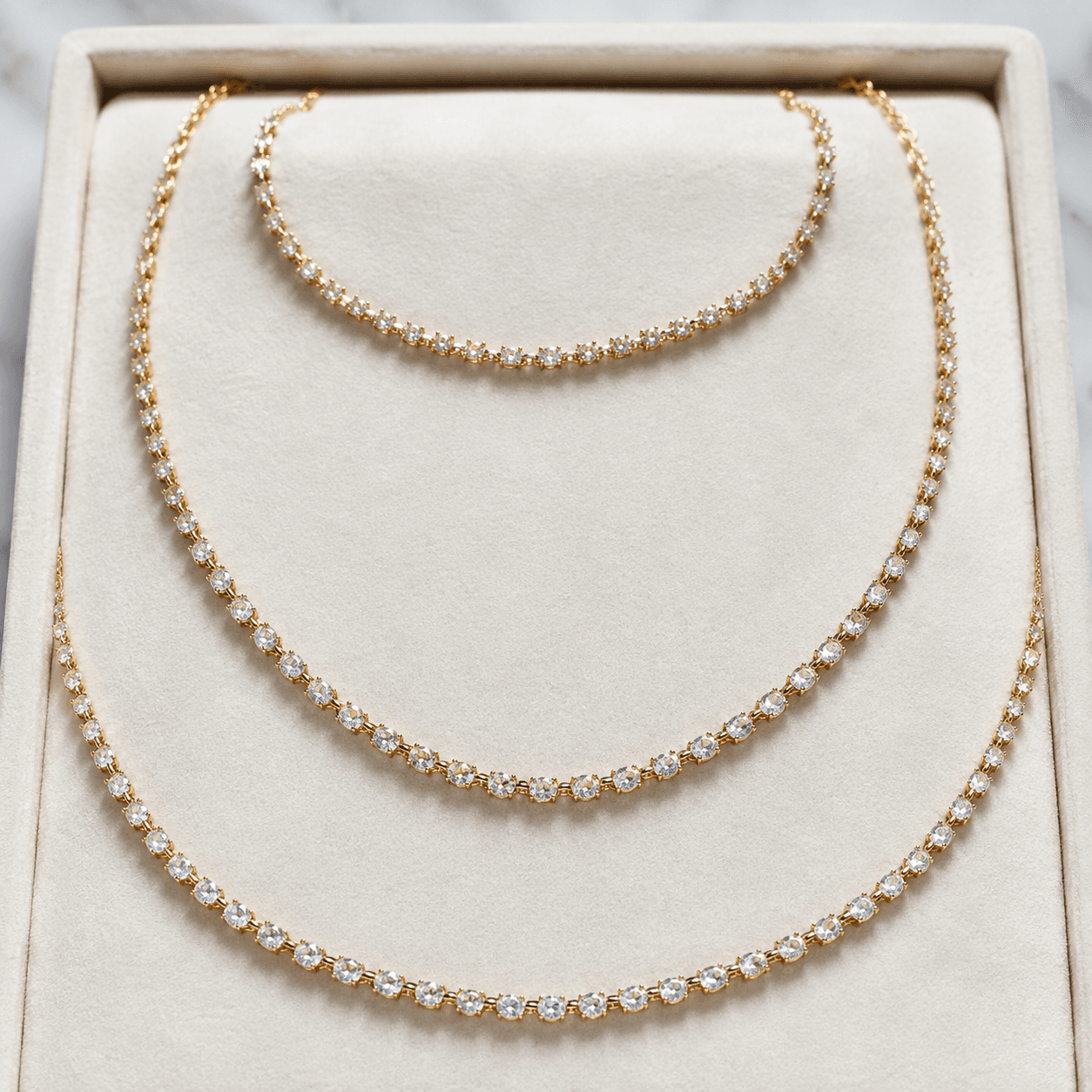A flat-lay of three necklaces in different lengths, choker, princess, and matinee, arranged on a white velvet tray, overhead