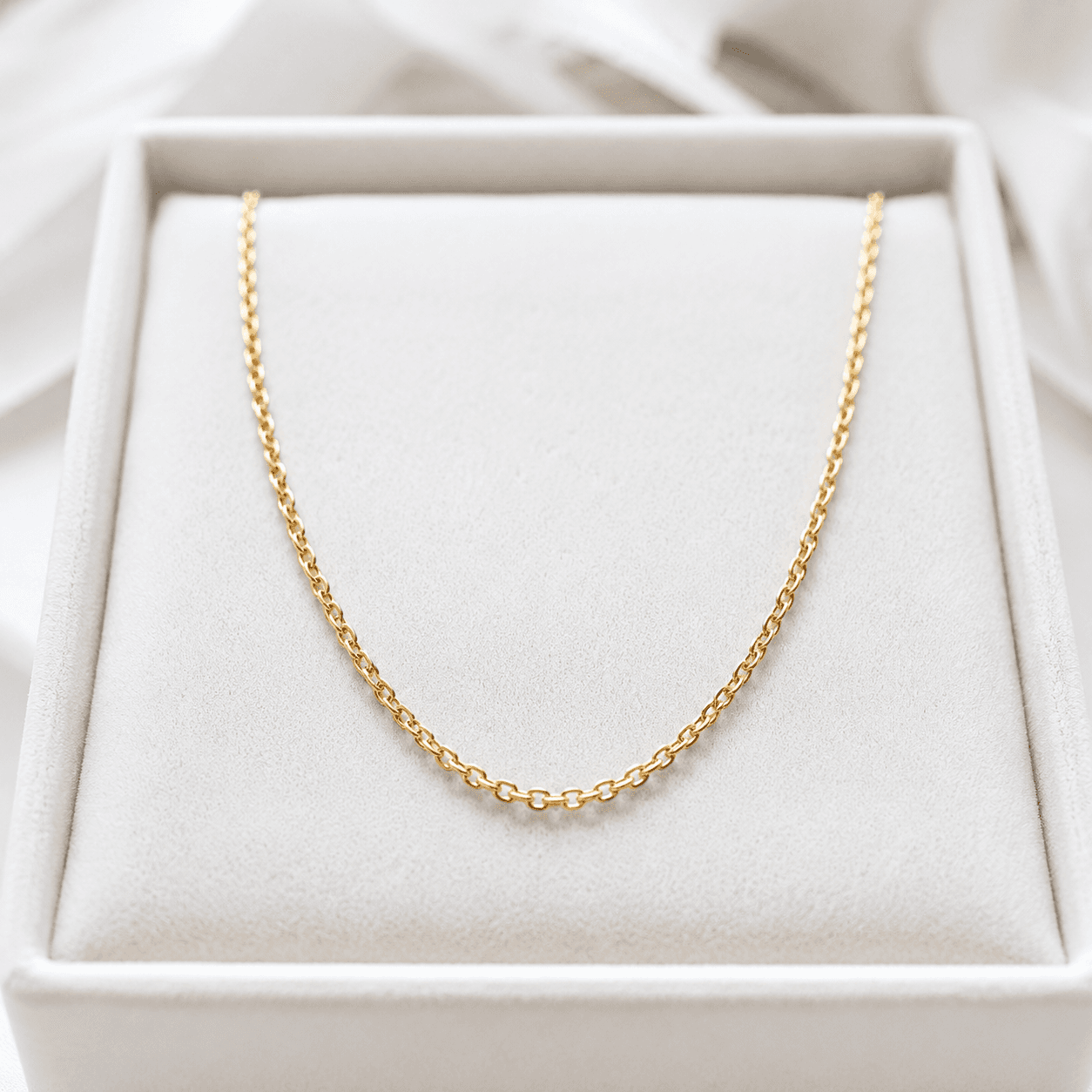 A close-up of a delicate gold chain necklace laid flat on a white velvet jewelry tray, soft studio lighting highlighting the