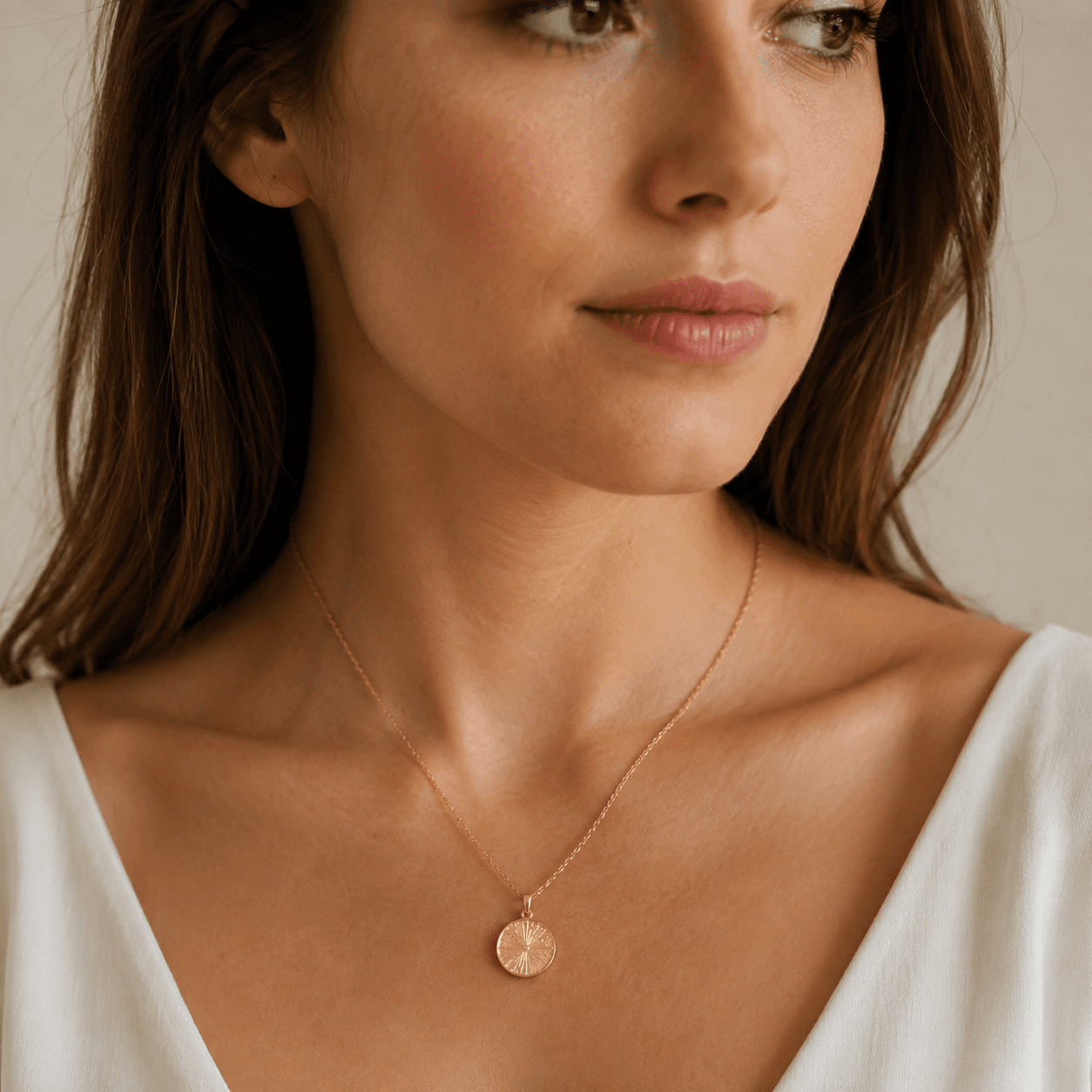 A woman wearing a perfectly fitted gold pendant necklace at collarbone length, soft natural light, elegant neutral