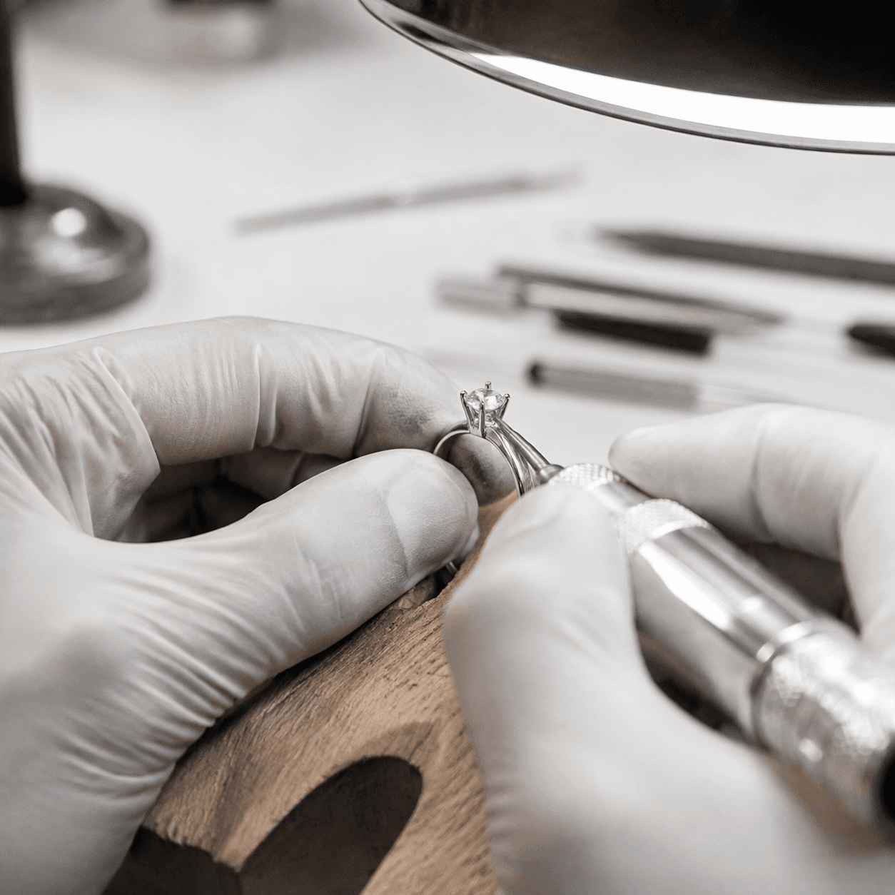 A jeweler's gloved hands carefully retipping a worn prong on a solitaire ring under a bright bench lamp, macro shot, clean