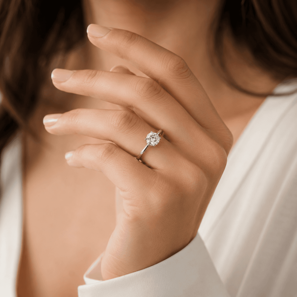 A woman's hand displaying a perfectly fitted diamond engagement ring, soft natural light, elegant neutral background