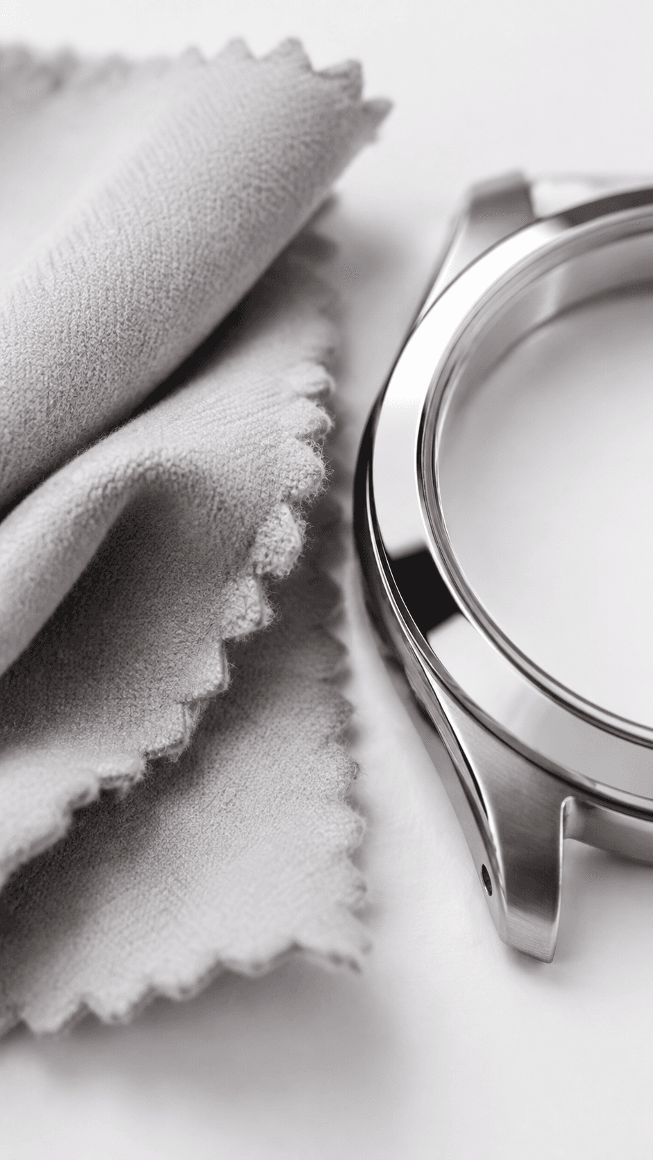 Polished stainless steel watch case beside a folded gray microfiber cleaning cloth