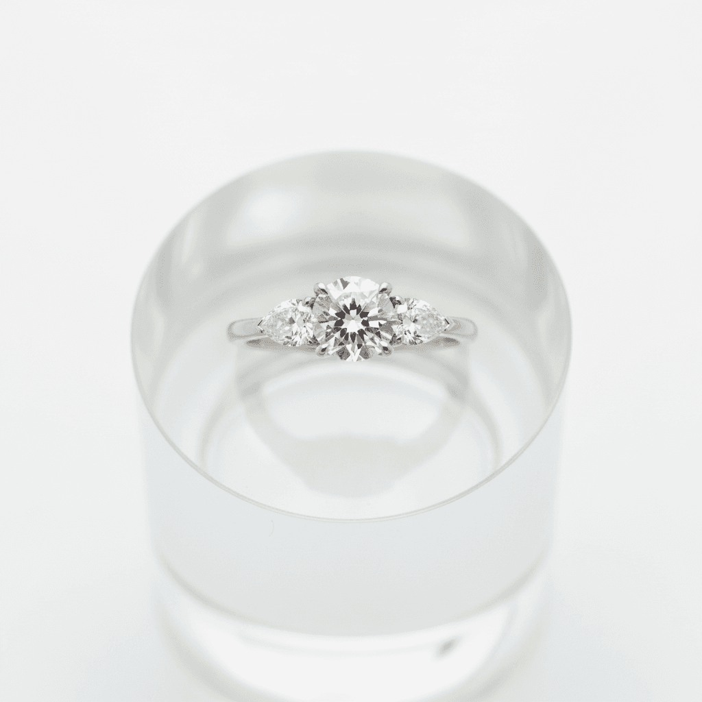 Three-stone diamond engagement ring with round center and pear side stones on white