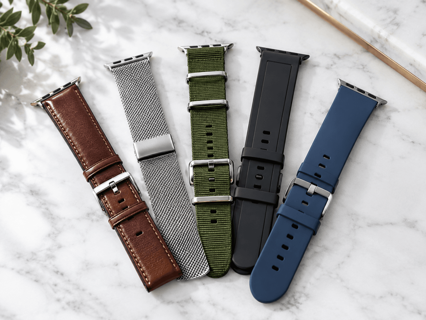 A flat lay of five different watch band styles, leather, stainless mesh, NATO fabric, rubber, and silicone, arranged in a
